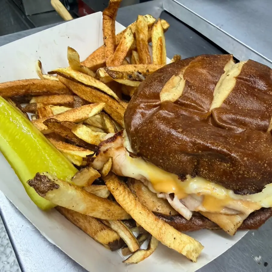 The Bennigan turkey sandwich on a pretzel bun with fries and a pickle spear